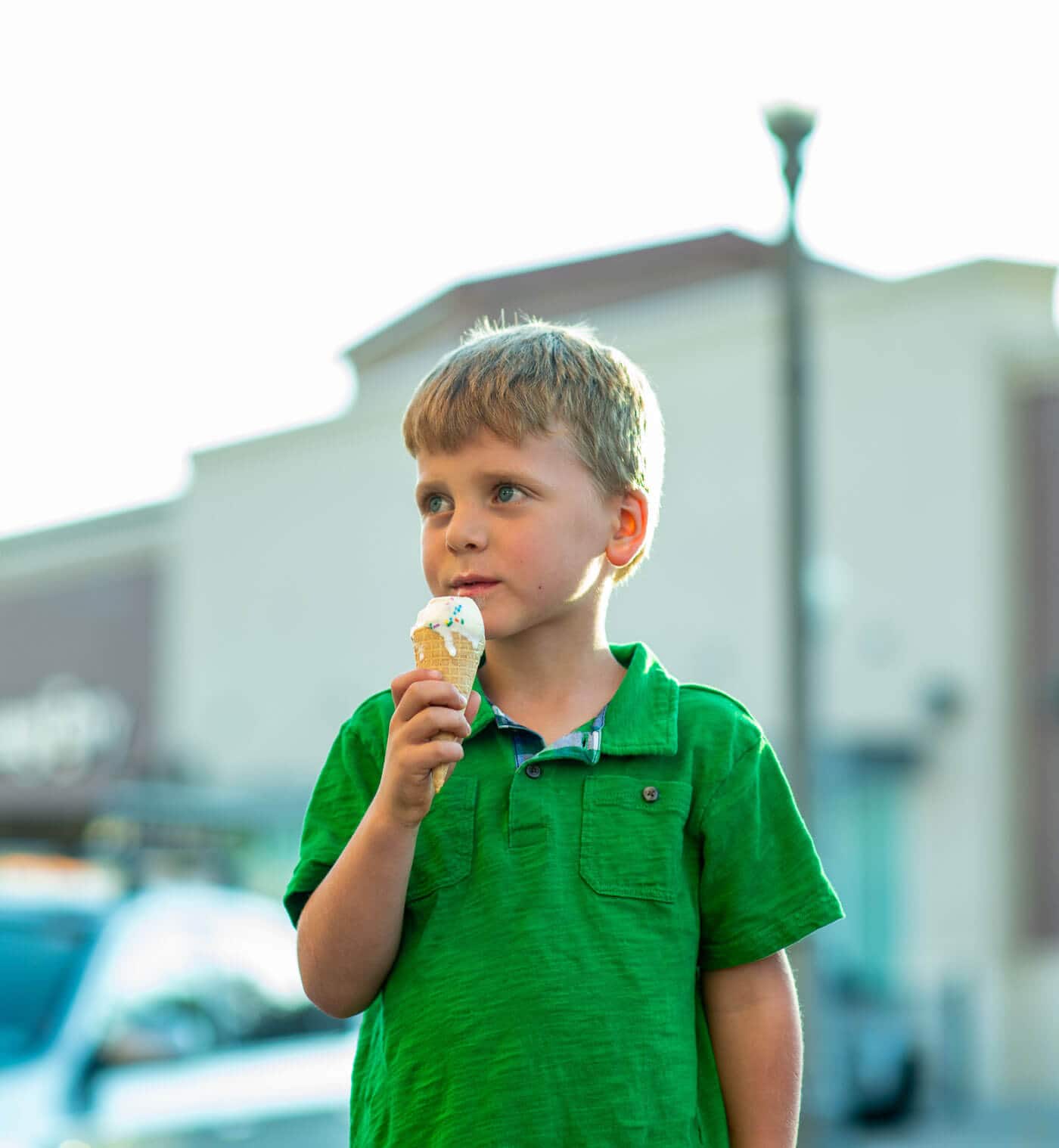 A kid in a green t-shirt eating a ice cream cone 