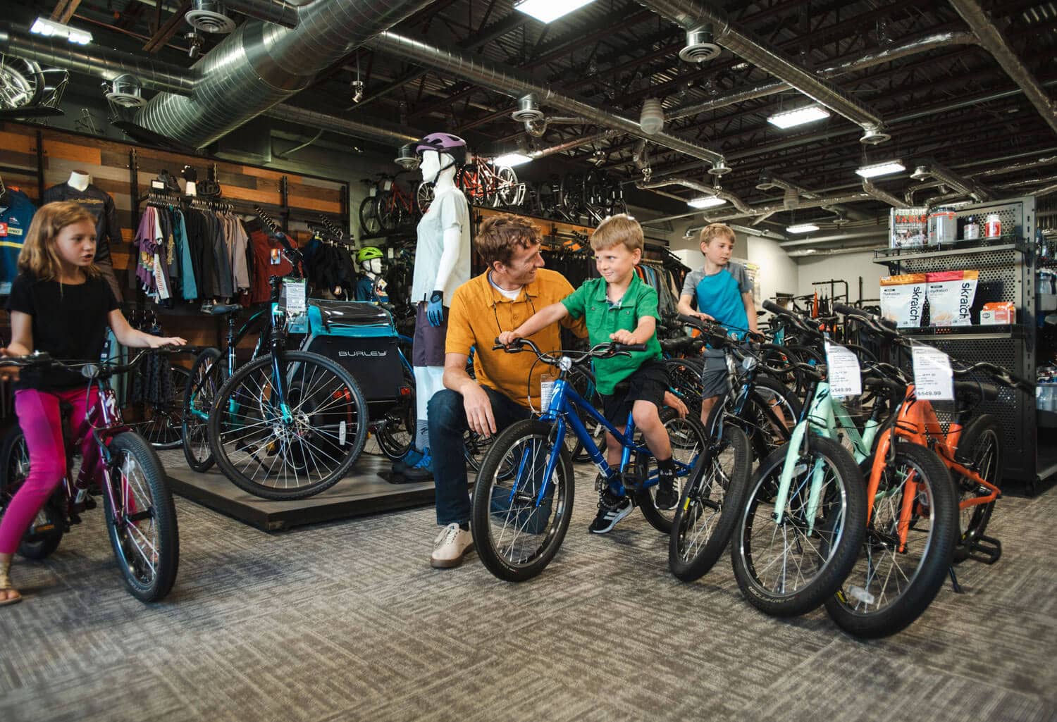 A family and kids are test-riding child bikes inside a bike shop