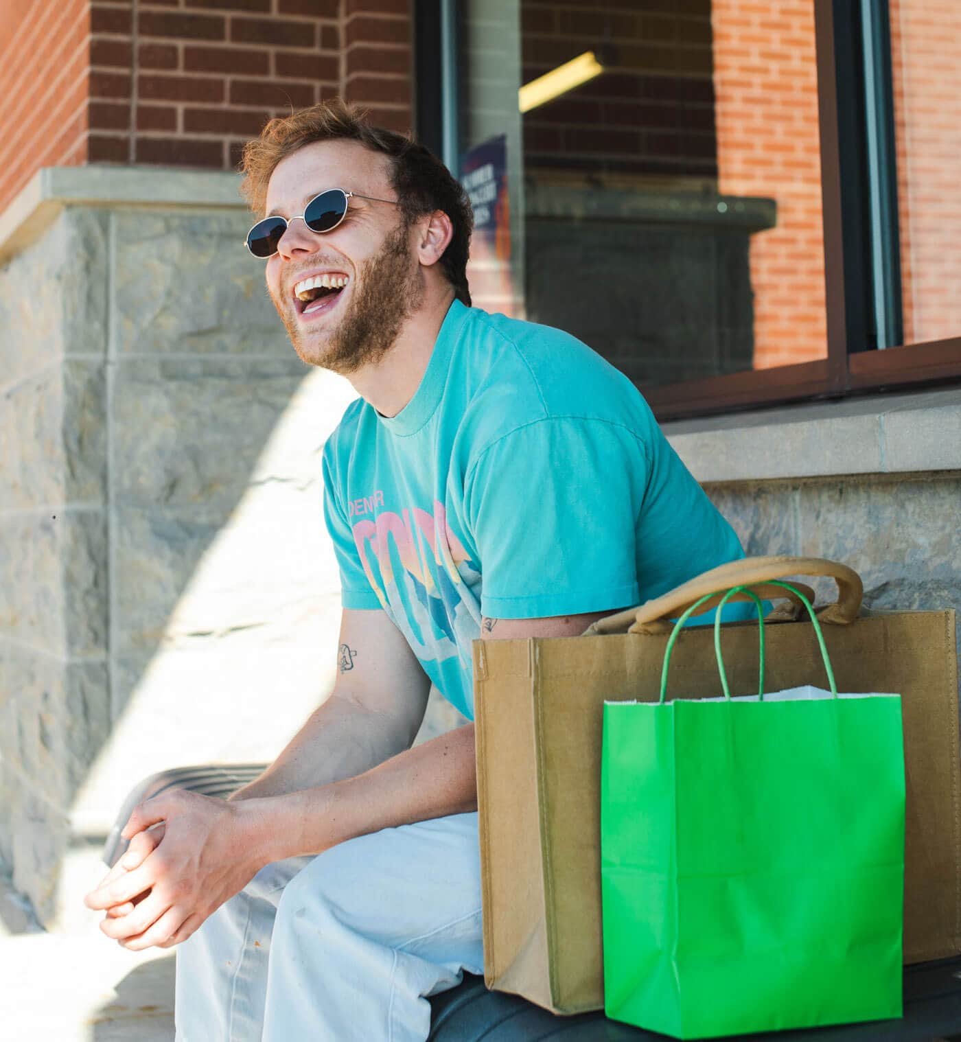 A man with sunglasses sitting on bench with shopping bags
